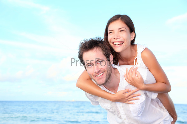 Happy beach couple doing piggyback having summer vacation fun. Young interracial couple, Asian woman, Caucasian man.