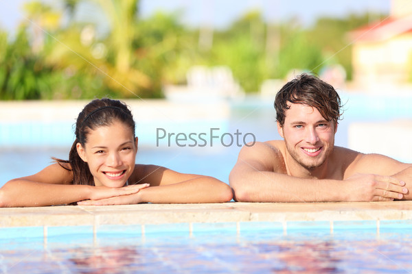 Young couple in pool - summer travel photo of two happy smiling people relaxing in tropical resort swimming pool. Caucasian man, Asian woman, focus on male model.