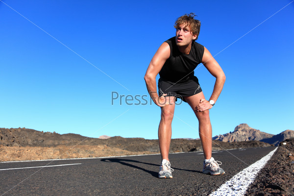 Jogger resting after running. Man runner taking a break during training outdoors in amazing landscape. Young Caucasian male fitness model after work out.