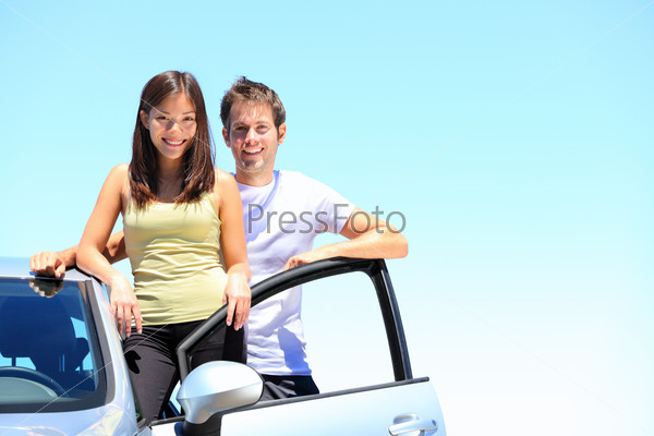 Couple and new car smiling happy standing outside on sunny summer day during road trip travel vacation Young interracial couple in their twenties, Asian woman, Caucasian man