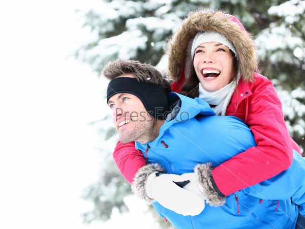 Winter couple piggyback in snow smiling happy and excited. Beautiful young multiracial couple, Asian woman, Caucasian man piggybacking