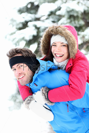 Happy winter couple piggybacking in snow smiling and joyful at camera. Beautiful young multi-ethnic couple, Asian mixed-race woman, Caucasian man doing piggyback.