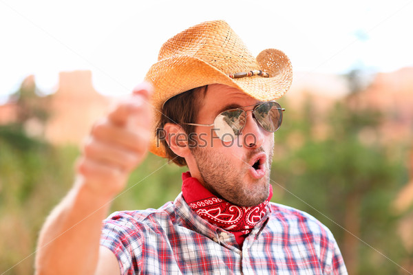 Cowboy man with sunglasses and cowboy hat pointing at camera saying WE WANT YOU. Male model in american rural western countryside landscape nature on ranch or farm, Utah, USA.