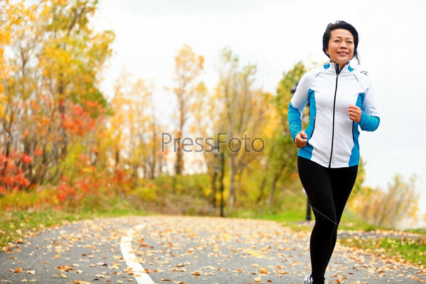 Mature Asian Woman Running Active In Her 50s. Middle Aged Female Jogging Outdoor Living Healthy Lifestyle In Beautiful Autumn City Park In Colorful Fall Foliage. Asian Chinese Adult In Her Fifties.