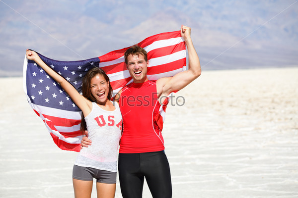 USA athletes people holding american flag cheering. Sports man and fitness runner woman celebrating winning after running. Happy young multicultural fitness couple in excited celebration outside.