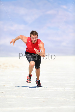 Runner - man running sprinting outdoor in desert nature. Fit athlete in fast sprint run at great speed towards camera. Male fitness model training and working out in amazing extreme desert landscape.