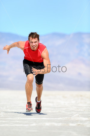 Running man - runner sprinting in desert nature. Fit athlete in fast sprint run at great speed towards camera. Male fitness model in amazing extreme desert landscape.