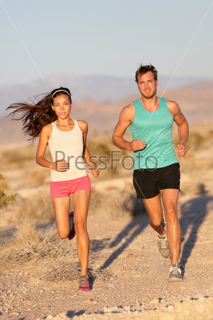 Running couple - runners jogging on trail run path outside in beautiful nature. Asian woman runner and Caucasian male fitness sport model jogger training together for cross-country marathon.