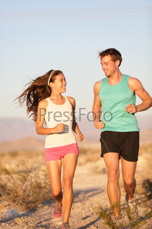 Runners - Active fitness couple running and laughing together outside. Happy runner woman and jogging man working out smiling during cross-country trail run. Asian female model and Caucasian male.