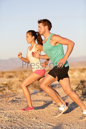 Runners couple running in trail run. Runner man and sport woman training and jogging outside in cross country run outside at summer sunset. Fit male Caucasian fitness model and Asian female runner.