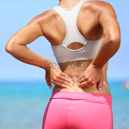 Back pain - woman having painful muscle injury in lower back. Fitness girl sport girl with sports injury outdoor on beach.