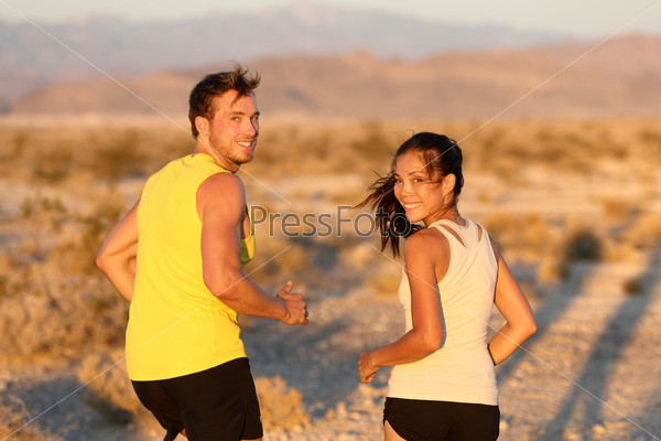 Exercise - couple running looking happy at camera. Runners jogging outside in cross-country trail run. Fit young athlete man and woman fitness runner training together in prairie nature landscape, USA