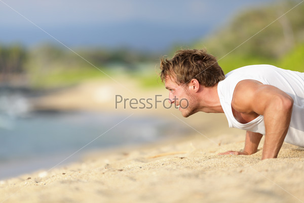 Push-ups - man fitness model training pushups on beach outdoors. Fit male fitness trainer working out exercising in summer on beach.