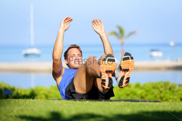 Fitness man doing sit-ups exercise for abs outdoors. Fit male athlete cross training jackknife sit up during workout. Muscular handsome young caucasian man working out outside.