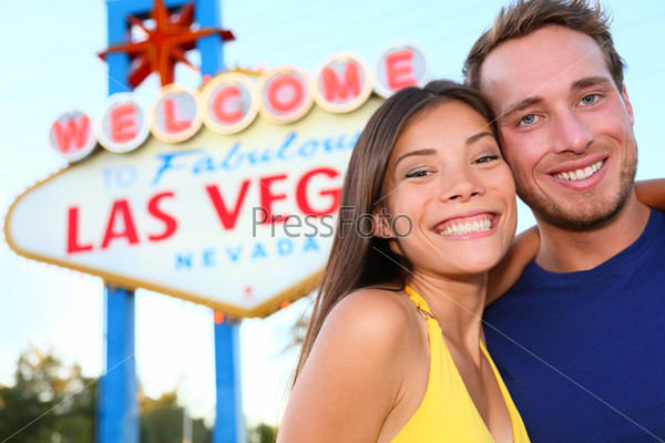 Las Vegas tourist couple at Las Vegas sign. Happy tourist couple taking self-portrait in front of Welcome to Fabulous Las Vegas sign. Beautiful young multi-ethnic people, Asian Woman, Caucasian man.