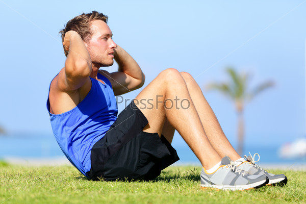 Sit-ups - fitness man training sit up outside in grass in summer. Fit male athlete working out cross training exercising. Caucasian muscular sports model in his 20s.