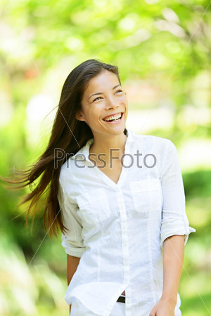 Joyful vivacious woman in a spring or summer park beaming a broad smile as she walks along rejoicing in the freshness of nature and the warm glow of the sunlight through the leaves of the green trees