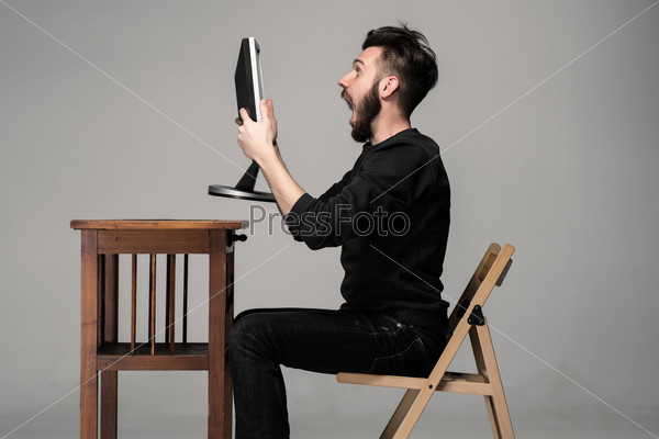 Funny and crazy man using a computer on gray background. man\'s hands holding a monitor. Concept of surprise and indignation