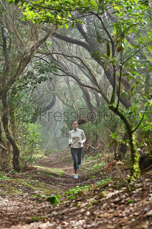 Runner woman cross-country running in beautiful forest trail run. Female athlete jogger training outdoor in amazing atmospheric forest nature landscape. Fit female fitness model with healthy lifestyle