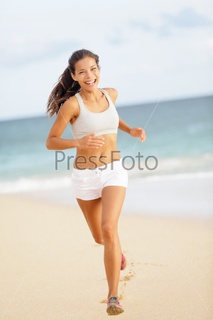 Runner woman running on beach smiling happy. Beautiful vivacious woman jogging on the beach in summer sport shorts laughing as she enjoys the exercise and sunshine. Asian fitness model exercising.