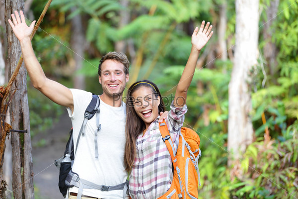 Happy hiking - hikers cheering joyful in forest. Cheerful excited hiker couple with arms raised up outstretched in joy smiling happy looking at camera. Multiethnic man and woman on Big Island, Hawaii.