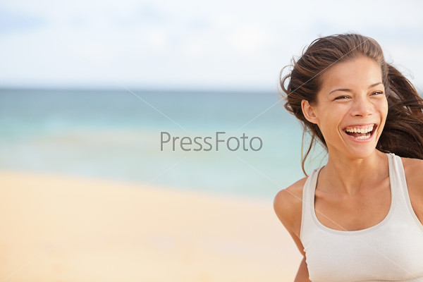 Beach fun - happy running woman closeup with copy space. Smiling joyful elated girl jogging and laughing while training outdoors on beautiful beach. Mixed race Asian Chinese / Caucasian female model.