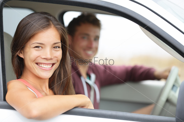 Cars - couple driving in new car smiling happy looking at camera. Young people on road trip drive in car. Beautiful interracial couple in their twenties, Asian woman, Caucasian man.