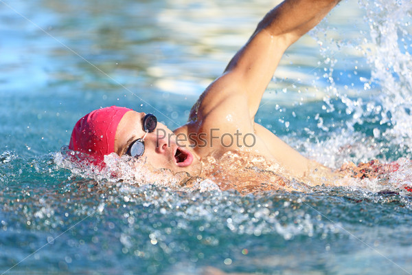 Man swimmer swimming crawl in blue water. Portrait of an athletic young male triathlete swimming crawl wearing a pink cap and swimming goggles while. Triathlete training for triathlon.