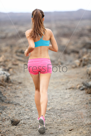 Trail runner woman running cross-country run training outside for marathon. Jogging female athlete working as part of healthy lifestyle. Rear view showing back from behind of woman runner on Hawaii.