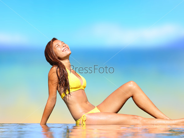 Sunbathing woman relaxing under sun in luxury spa retreat resort. Woman tanning enjoying sun in infinity pool in infinity pool by beach. Happy smiling mixed race Asian Caucasian girl in bikini, Hawaii