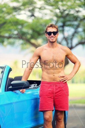 Handsome man with sports car. Well built fit young male model standing shirtless leaning on the door of a blue sports car smiling at the camera.
