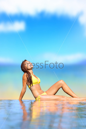 Pool woman in bikini. Holiday travel image of beautiful young woman in bikini sitting by pool smiling happy in tropical beach resort. Beautiful mixed race Caucasian Asian female bikini model