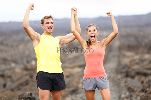 Cheering celebrating happy fitness runner couple with arms raised up in winning gesture expression outdoors