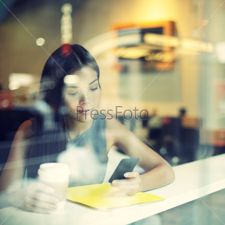 Cafe city lifestyle woman on phone drinking coffee texting text message on smartphone app sitting indoor in trendy urban cafe. Cool young modern mixed race Asian Caucasian female model in her 20s.