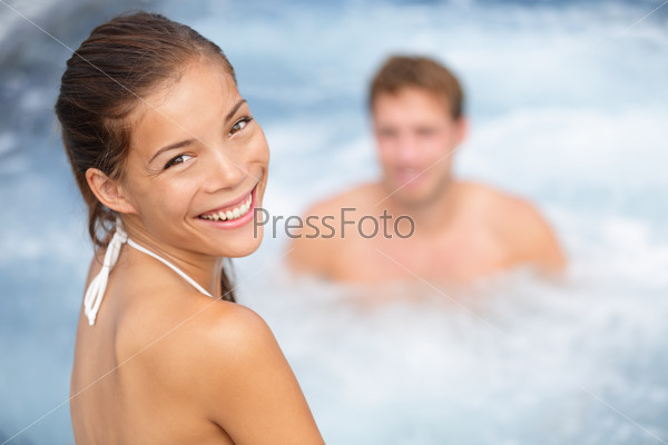 Spa resort jacuzzi hot tub couple, woman and man. Girl enjoying water in outdoor whirlpool smiling happy at camera during relaxing vacation holidays retreat. Multiethniic young couple, Asian woman.