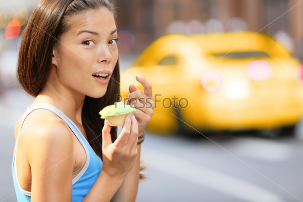 Cupcakes - woman caught eating cupcake snack after running training. Funny image of fitness girl surprise shocked looking at camera eating unhealthy food. Beautiful woman in New York City, Manhattan.