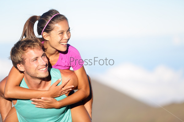 Happy young couple piggybacking outside. Fitness woman and man in love smiling excited having fun together outdoors in nature looking to side at copy space. Mutiethnic couple, Asian and Caucasian.