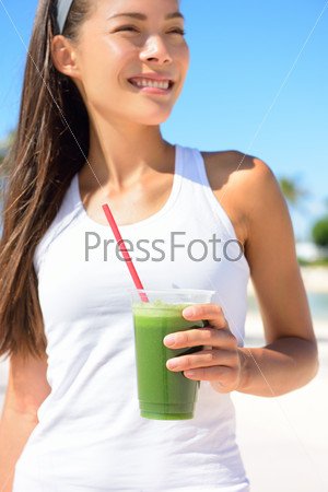 Green smoothie. Woman holding green vegetable detox juice outside in summer sun. Healthy lifestyle with beautiful mixed race Asian Caucasian female model taking a cleanse diet.