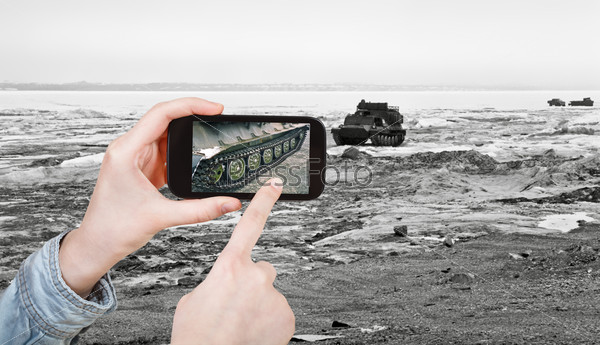 travel concept - tourist taking photo of tracked vehicle on ice road on mobile gadget, Anadyr, Chukotka, Russia