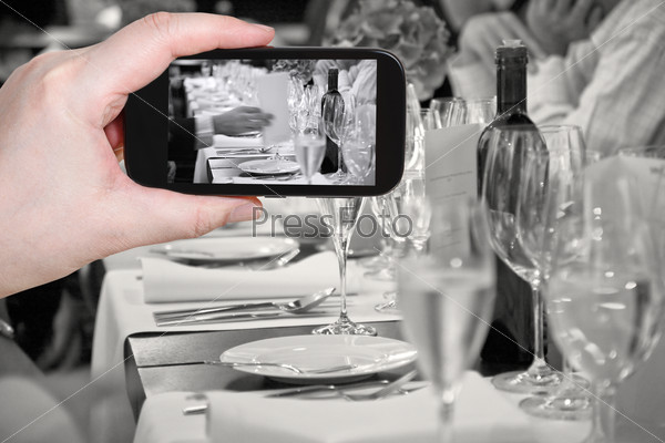 photographing food concept - tourist takes picture of beginning of official dinner in restaurant on smartphone,