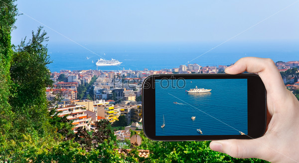 travel concept - tourist taking photo of ships near Cannes town on mobile gadget, France