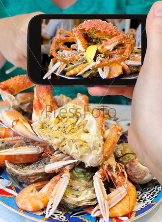 photographing food concept - tourist takes picture of seafood plate with crab, prawns, shrimps on smartphone, France