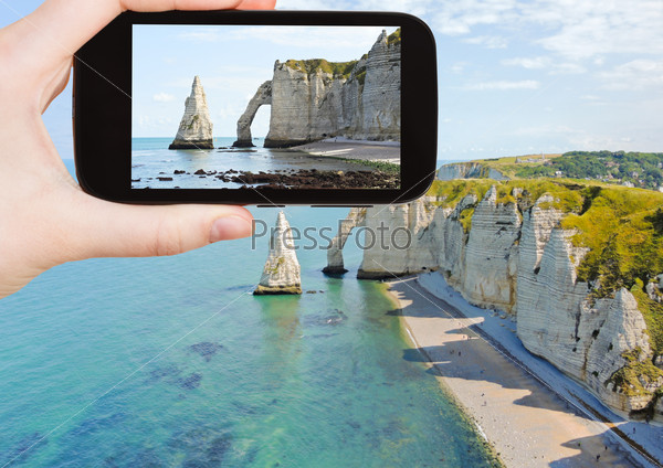 travel concept - tourist taking photo of english channel coast with cliffs on Etretat cote d\'albatre, France on mobile gadget