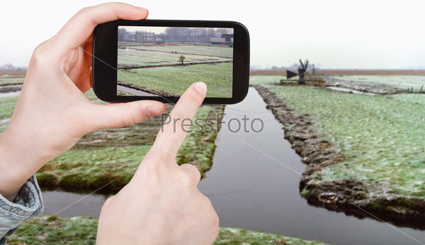 travel concept - tourist taking photo of frozen canals in Netherlands in winter on mobile gadget