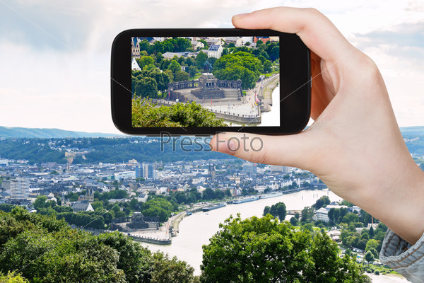 travel concept - tourist takes picture of Deutsches Eck (German Corner) at the confluence of Moselle and Rhine rivers in Koblenz town , Germany on smartphone,
