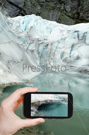 travel concept - tourist taking photo of water under in briksdal glacier in Norway on mobile gadget