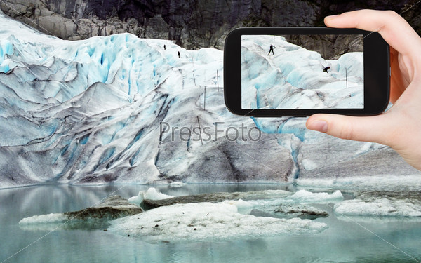travel concept - tourist taking photo of people on briksdal glacier in Norway on mobile gadget