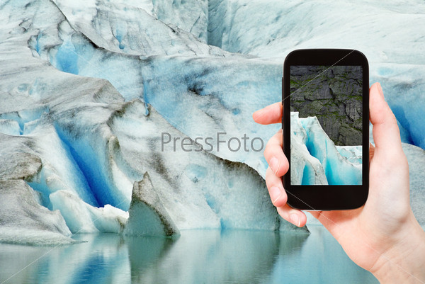 travel concept - tourist taking photo of melting snow in briksdal glacier in Norway on mobile gadget