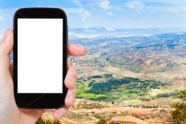 travel concept - tourist photograph Promised Land from Mount Nebo in Jordan on smartphone with cut out screen with blank place for advertising logo