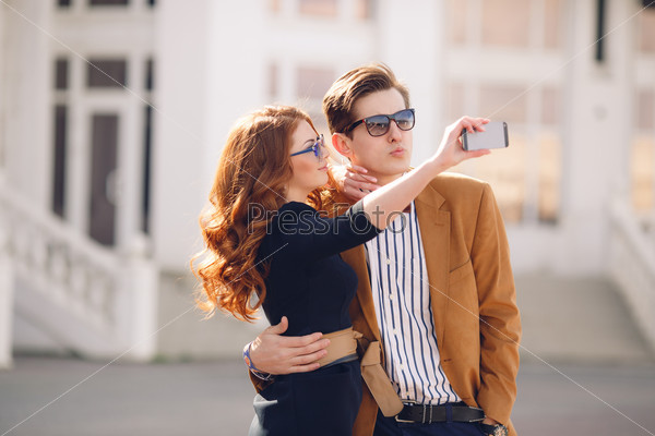 summer holidays, technology, love, relationship and dating concept - smiling couple taking selfie with smartphone in the city. Couple taking photograph of themselves kissing with a smartphone outdoors